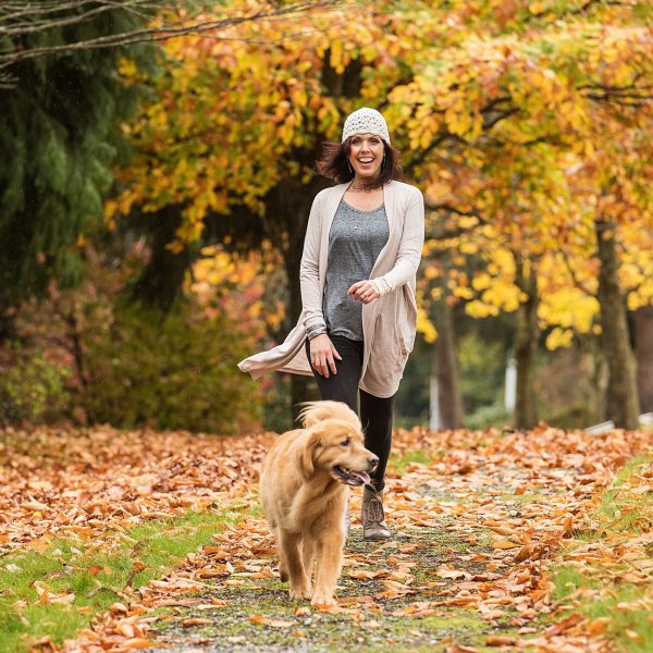 Happy woman walking her Golden Retriever Dog in a park with Fall